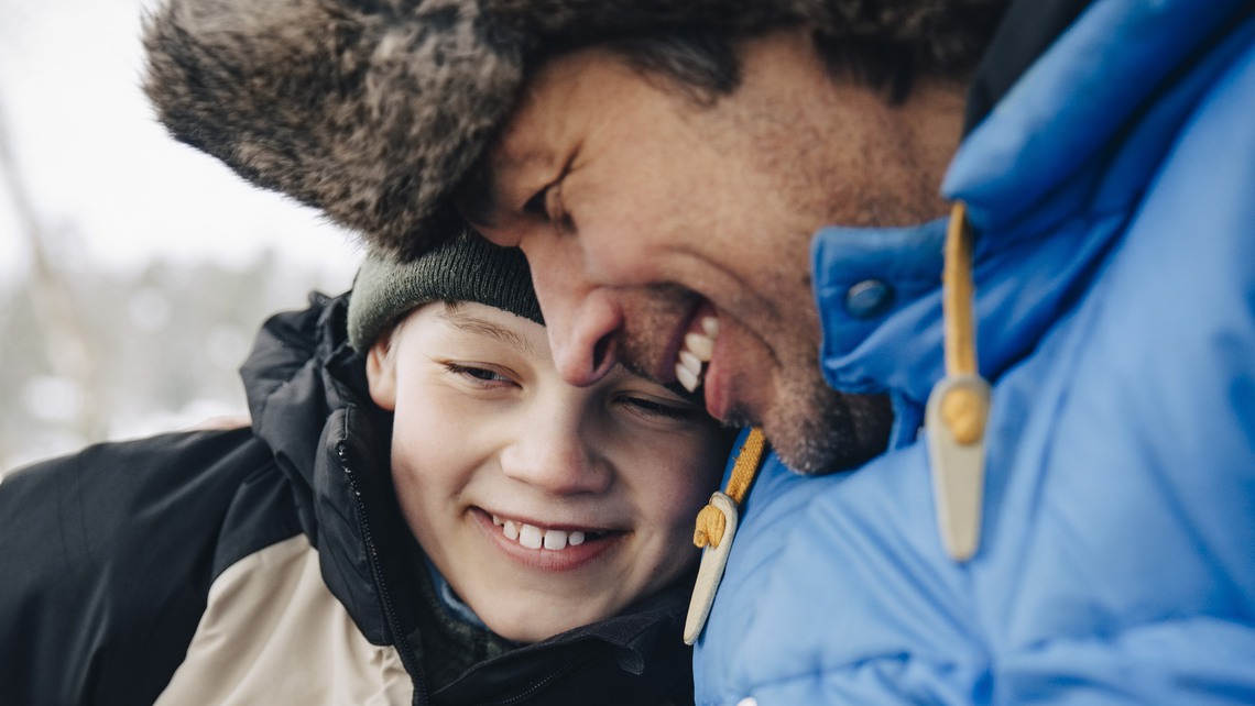 Happy father holding cup of tea embracing son in warm clothing