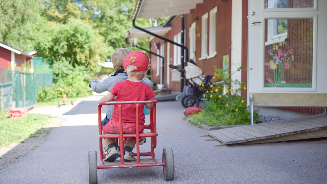 Ett förskolebarn i röda kläder cyklar på en röd cykel. 
