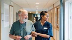 Smiling senior man walking arm in arm with female nurse while looking away in alley at nursing home