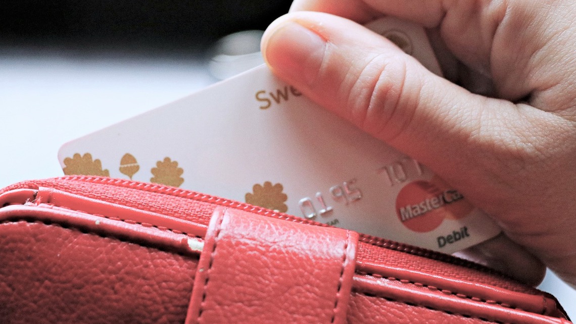 En hand håller i ett betalkort och en röd plånbok. 