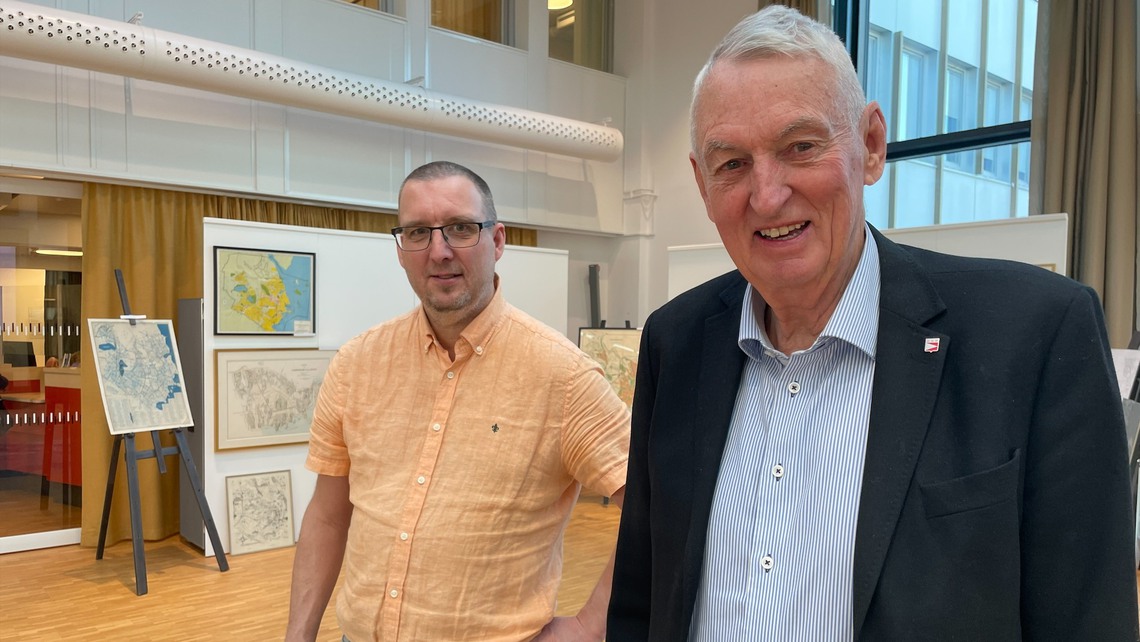 Några män som står bredvid varandra. Kartor på en vägg bakom.