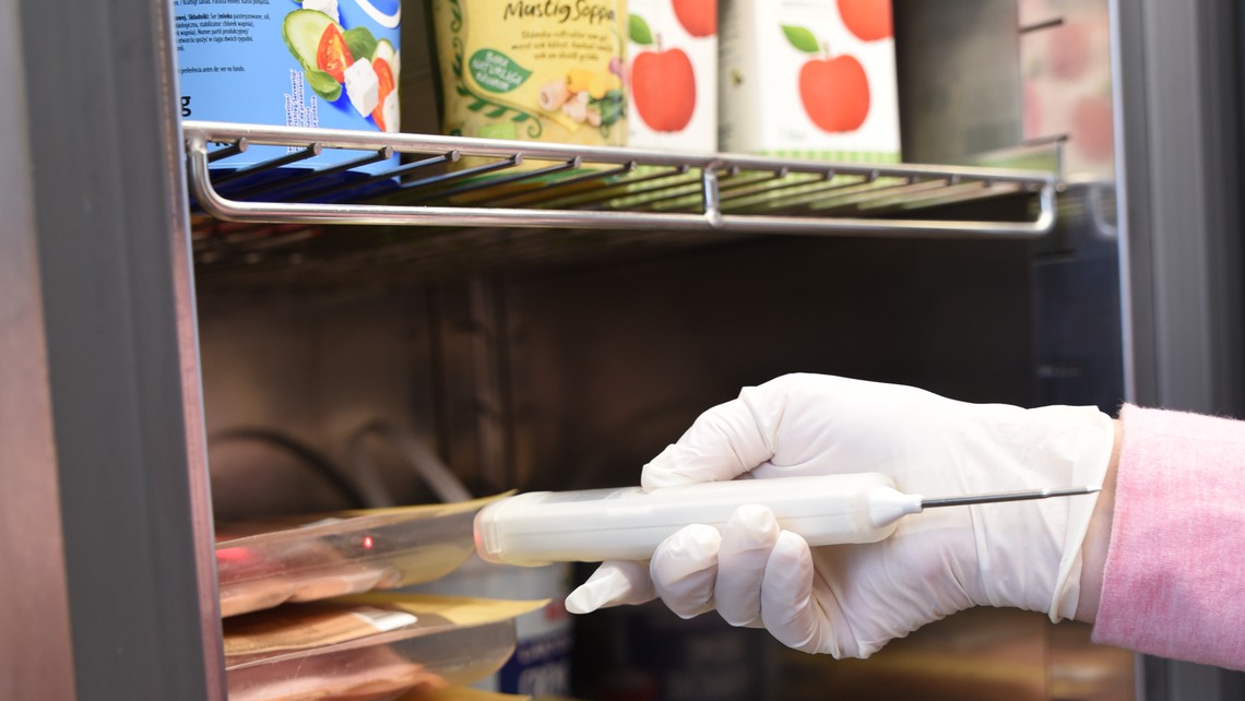 Miljö- och hälsoskyddsinspektör tar tempen i ett kylskåp.