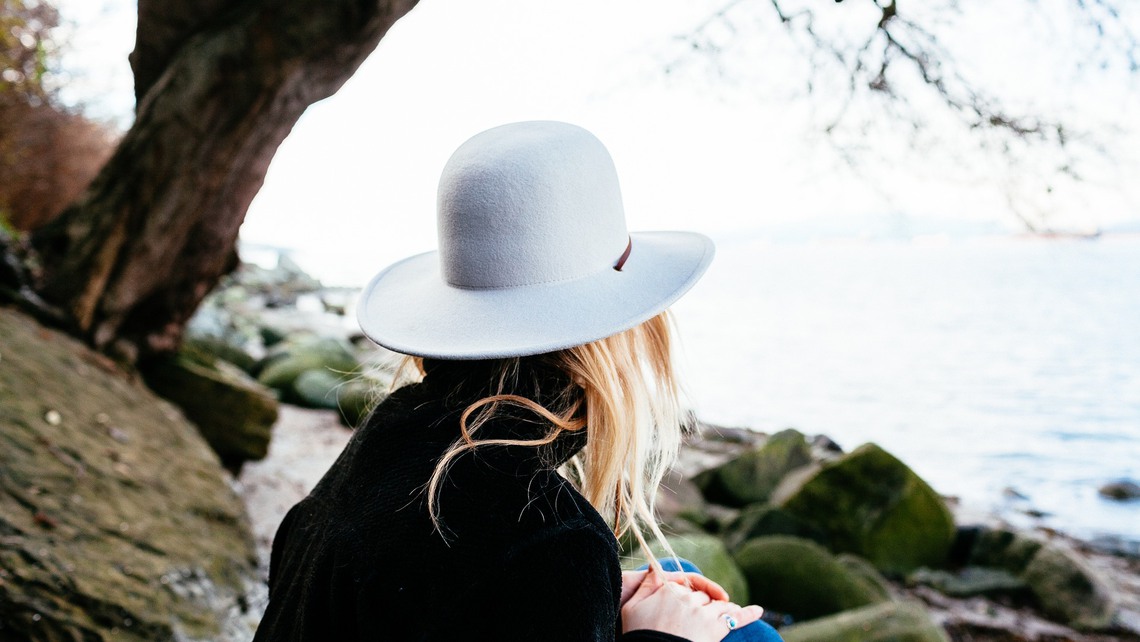 En kvinna sitter med en hatt och blickar ut över havet. 
