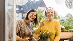 Happy woman and mother-in-law holding potted plant in balcony