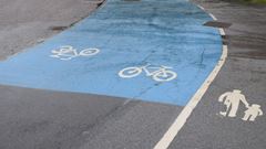 En blåmålad cykelbana intill en gångbana med linje emellan.