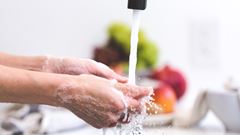 En person tvättar händerna under rinnande vatten från vattenkran i kök.