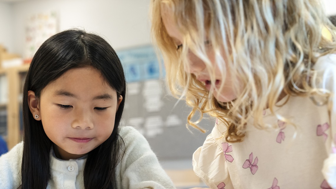 Girls assisting each other while studying together in classroom at elementary school