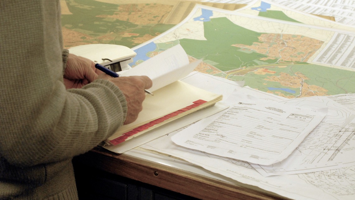 En man bläddrar i en pärm med ett arkiv av ritningar. 