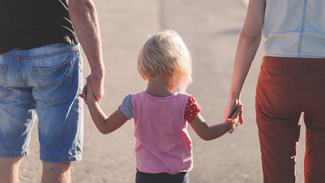 Två föräldrar håller sin dotter i handen. 