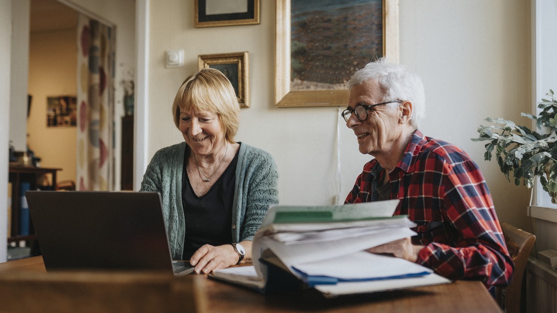 Äldre par vid köksbord med dator och pärm