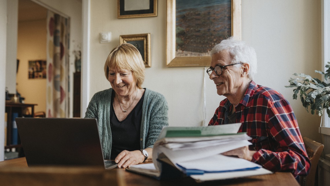 Äldre par vid köksbord med dator och pärm
