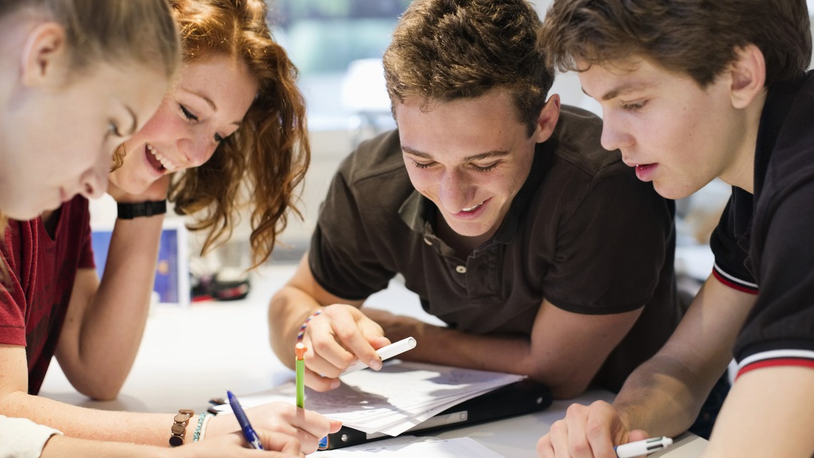 Happy young students studying together at table