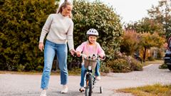 Flicka cyklar med mamma i bakgrunden