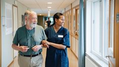 Smiling senior man walking arm in arm with female nurse while looking away in alley at nursing home
