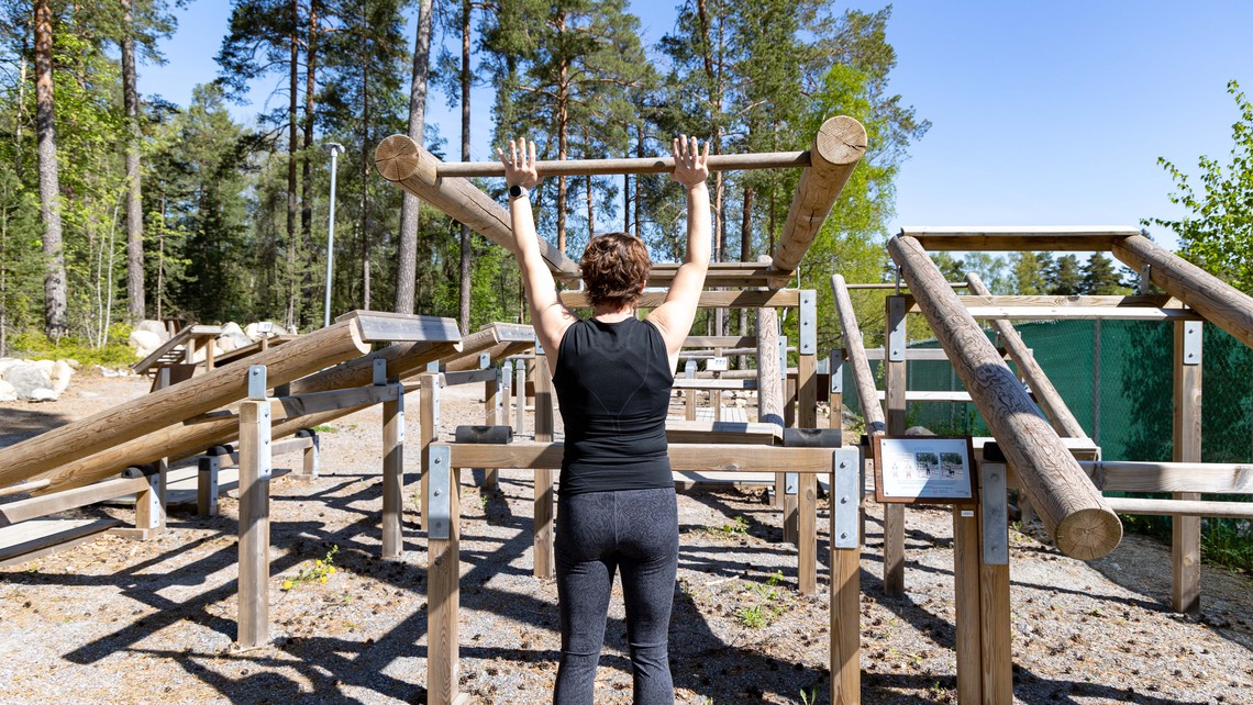 En tjej lyfter stockar vid ett utegym.