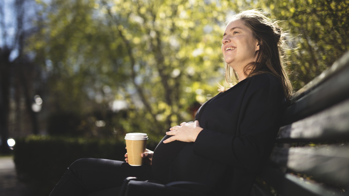 Gravid kvinna dricker kaffe på bänk